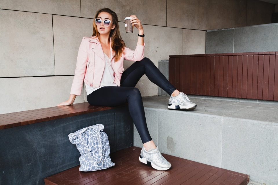 young beautiful stylish hipster woman in pink leather jacket, glam rock style, summer trend outfit, sunglasses, positive mood, happy, smiling, sexy, drinking coffee in paper cup